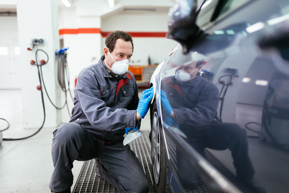 Detailer in a mask applying ceramic coating along the side panel of a dark car
