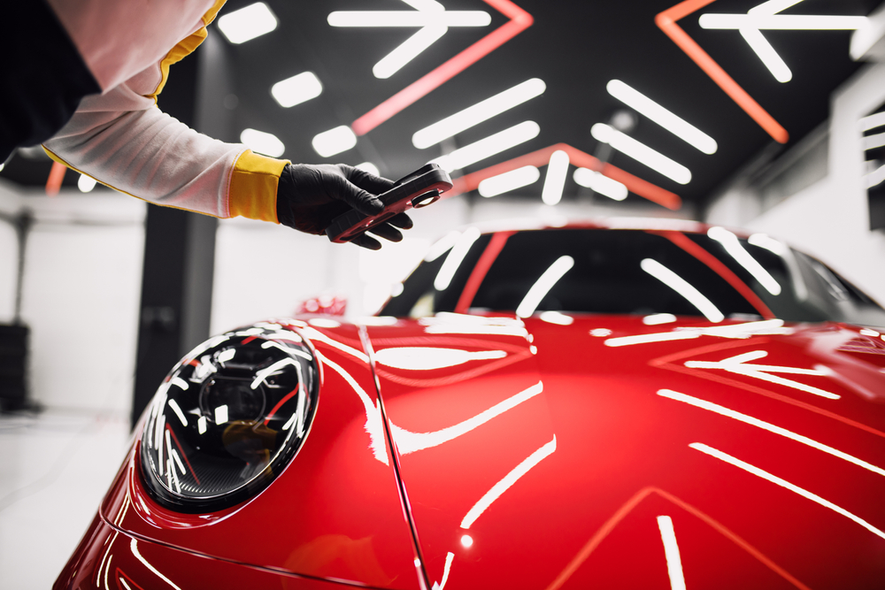 Detailer inspecting the glossy bonnet of a red sports car under studio light bars in Newcastle