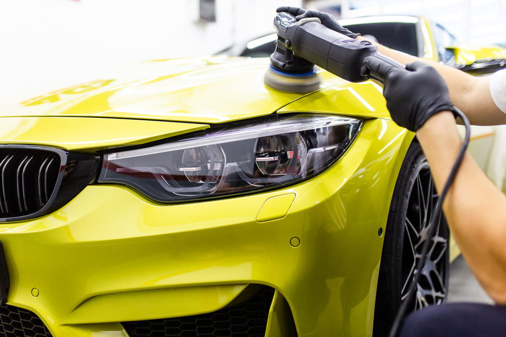 Machine polisher correcting paintwork on a bright sports car bonnet
