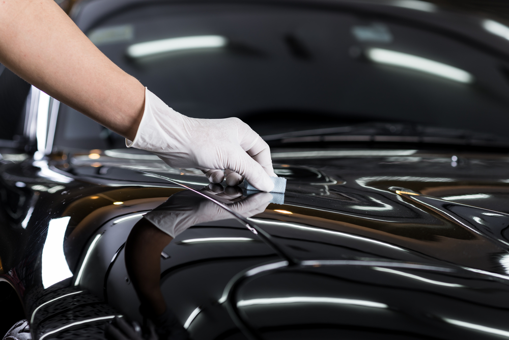 Gloved hand applying ceramic protection by hand to a glossy black car bonnet