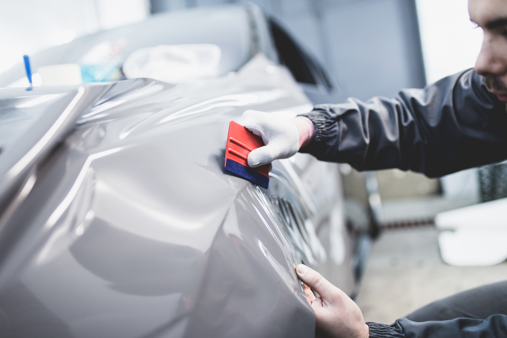 Detailer smoothing protective film onto a car panel with a squeegee at the Broadmeadow studio