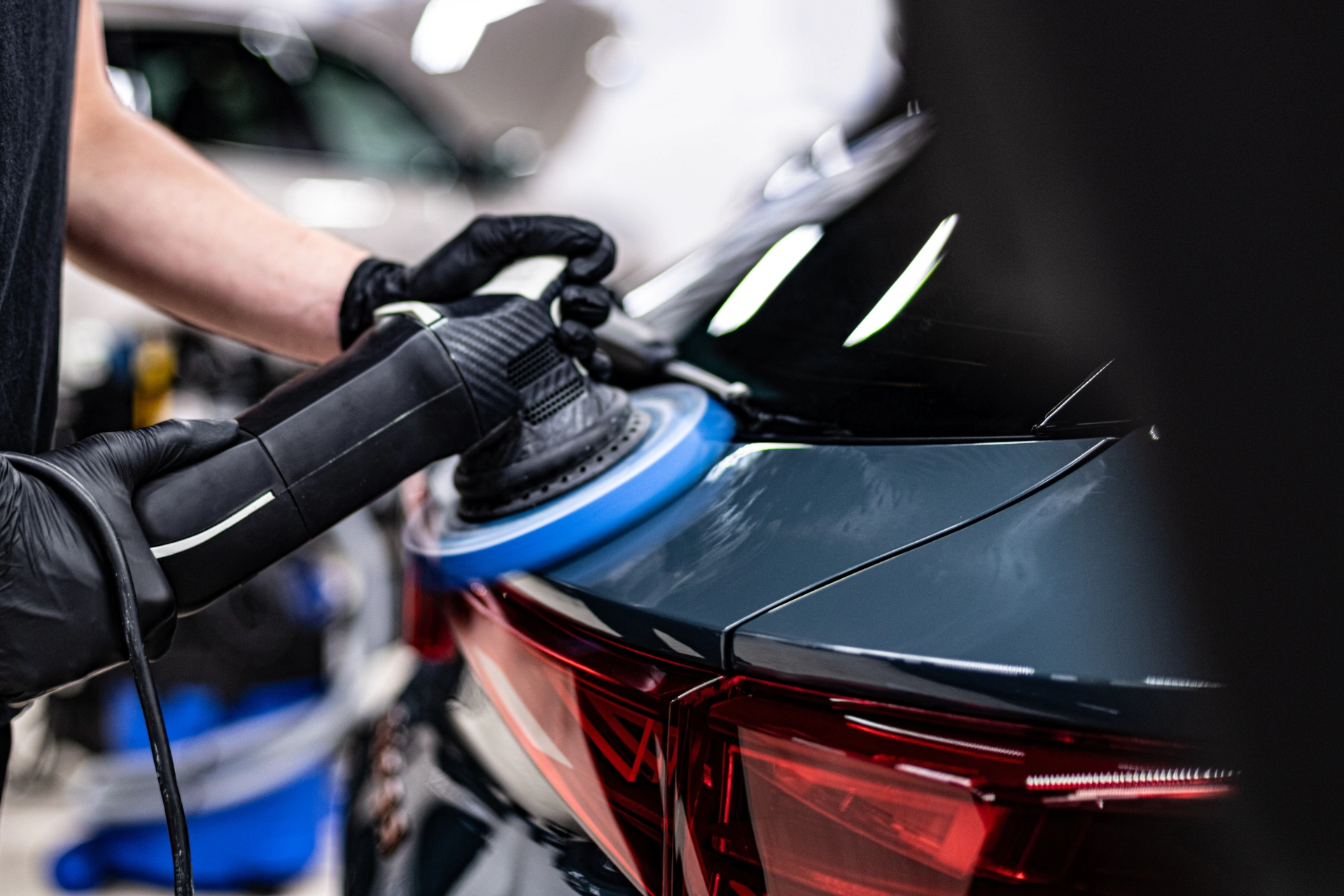 Detailer working a squeegee along the rear panel of a white performance car during paint correction