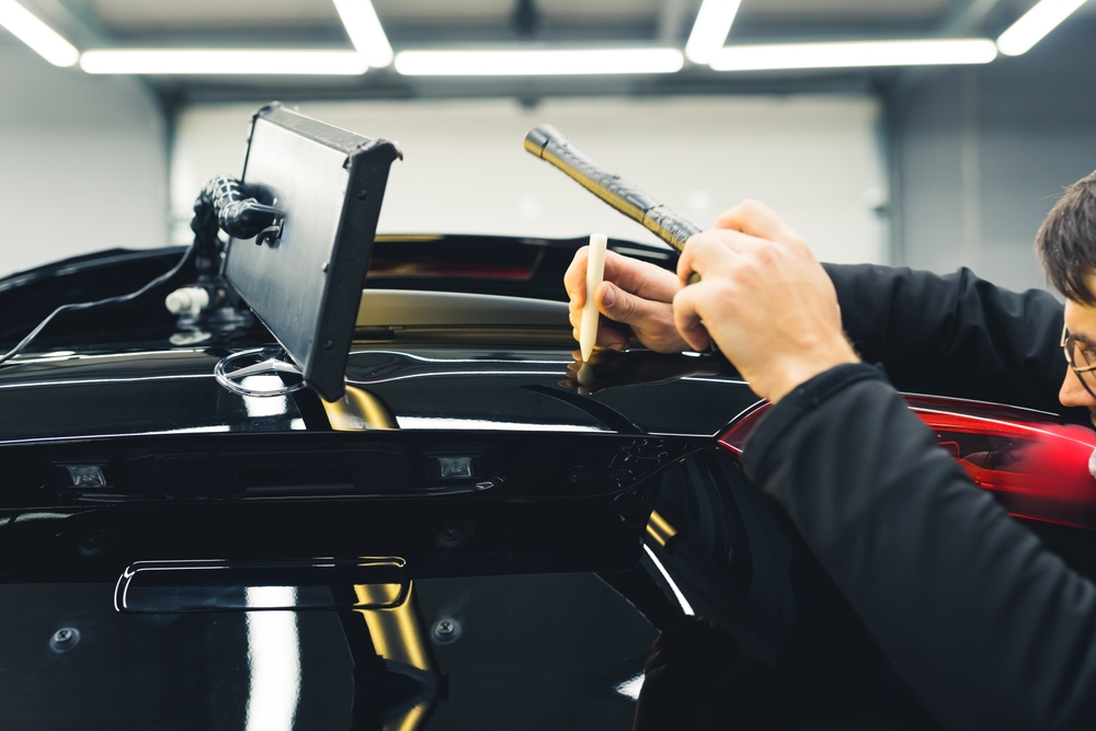 Detailer carefully working on the rear of a glossy black car in the Broadmeadow detailing workshop