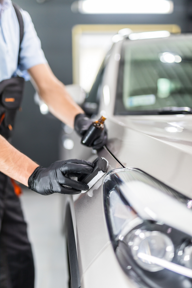 Detailer hand-applying ceramic coating with an applicator block to a silver car front panel