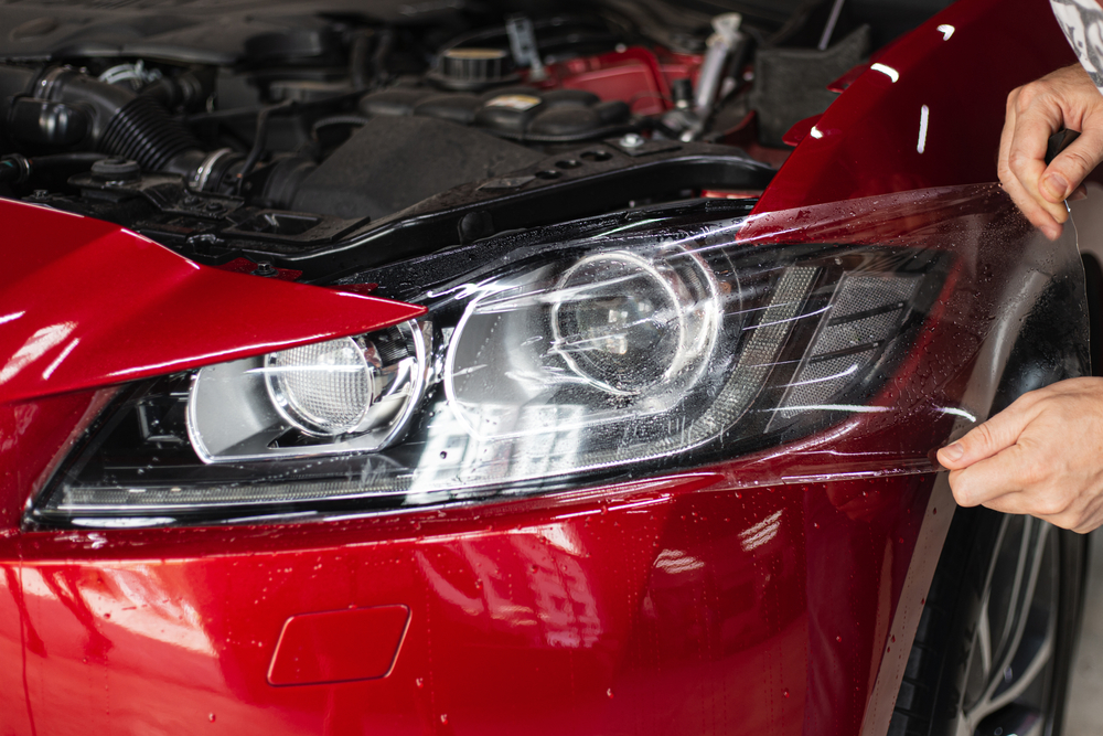 Detailer applying protective film over the headlight of a red car at the Broadmeadow detailing studio
