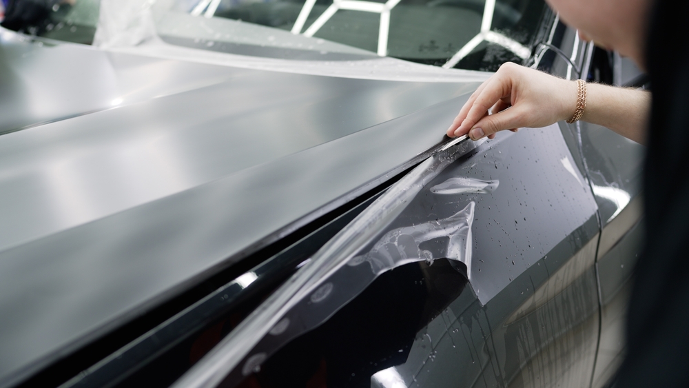 Detailer applying protective film to a dark car panel at the Broadmeadow detailing studio